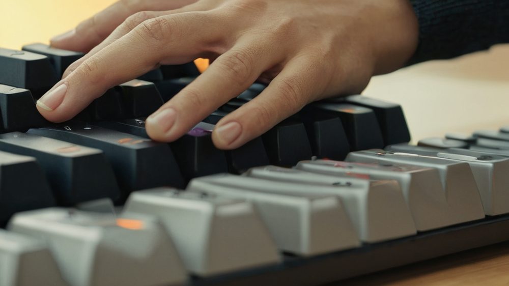A close-up of a hand hovering over a mechanical keyboard with shallow depth of field, focusing on the tension between hu